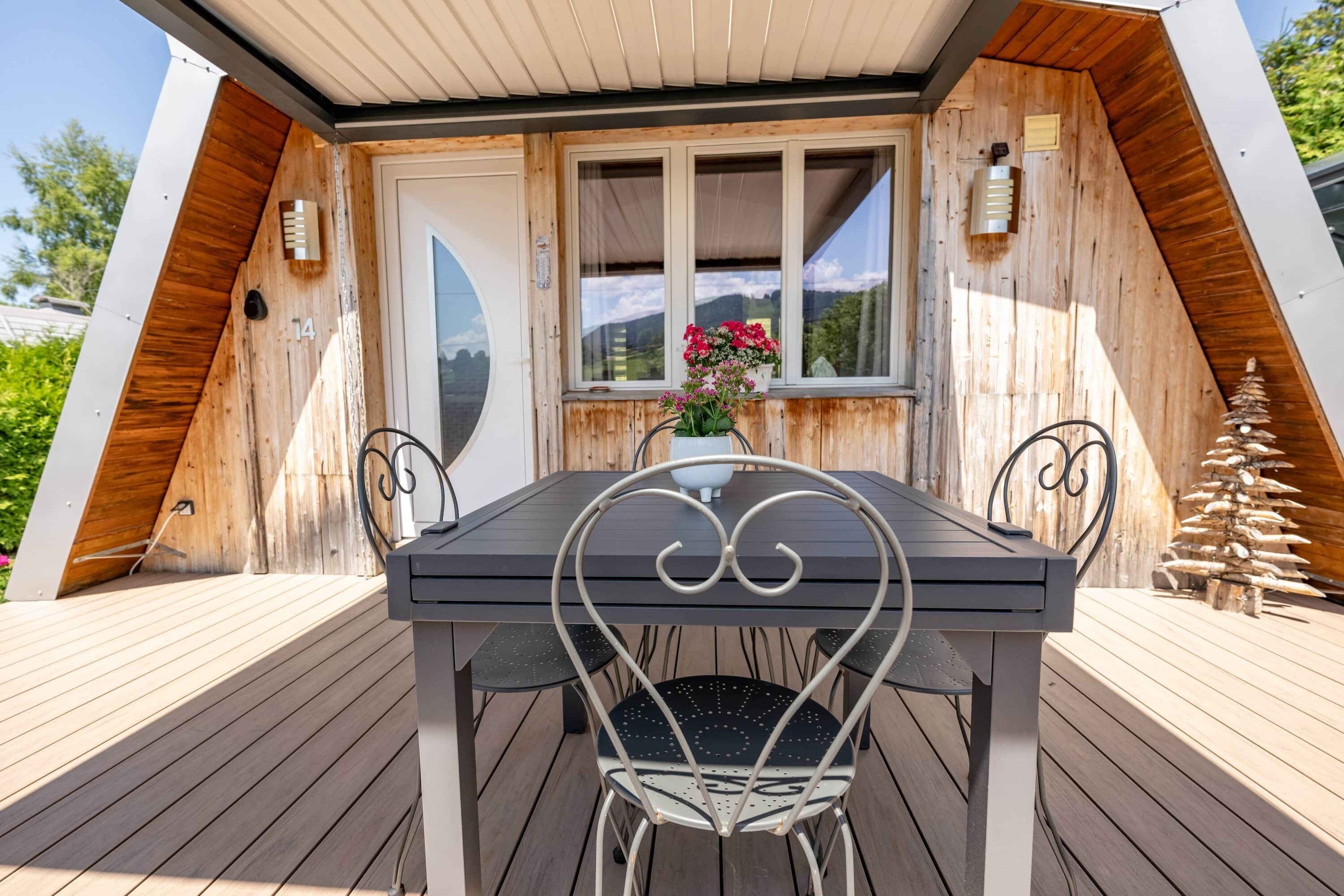 Een houten terras met een tafel en stoelen, een raam met uitzicht en een kleine plant in een pot.
