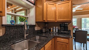 A kitchen with granite countertops, stainless steel sink, wooden cabinets, and a dining area with a table and chairs. - Lakefront Home | Private Dock, Hot Tub & Kayaks (Murray)