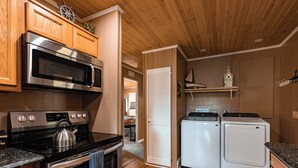 A compact kitchen with wooden cabinets, a stainless steel stove, an oven, a microwave, and a washing machine. - Lakefront Home | Private Dock, Hot Tub & Kayaks (Murray)