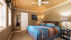 A bedroom with a wooden ceiling, a bed with a colorful bedspread, a nightstand with a lamp, and a wall-mounted TV. - Lakefront Home | Private Dock, Hot Tub & Kayaks (Murray)