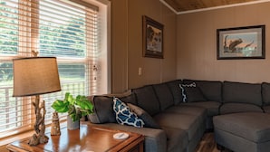 Un salon chaleureux avec un canapé d’angle, une lampe, une plante et deux tableaux encadrés au mur.