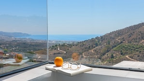 Une vue depuis une fenêtre d’un immeuble de grande hauteur, donnant sur une vallée avec des champs en terrasses et un plan d’eau situé au loin.
