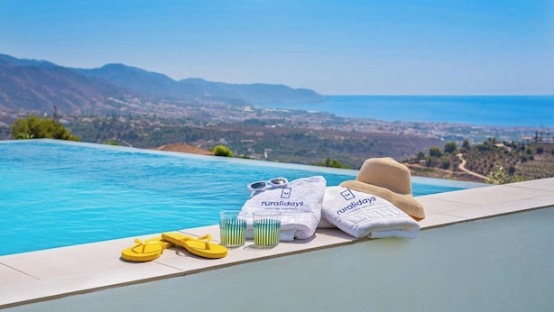 Une vue sur la piscine, avec un paysage magnifique sur l’océan et les montagnes en arrière-plan, et des équipements à disposition comme des serviettes, des sandales et un chapeau.