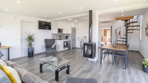 Un salon moderne avec une table basse en verre, un canapé gris et un coin repas comprenant une table et des chaises en bois.