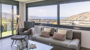 Un salon moderne avec une grande fenêtre, un canapé avec des coussins, un fauteuil et une table basse en verre.