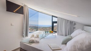 Une chambre d’hôtel avec un grand lit, une table de chevet sur laquelle se trouve une assiette de fruits, et une vue sur le paysage.