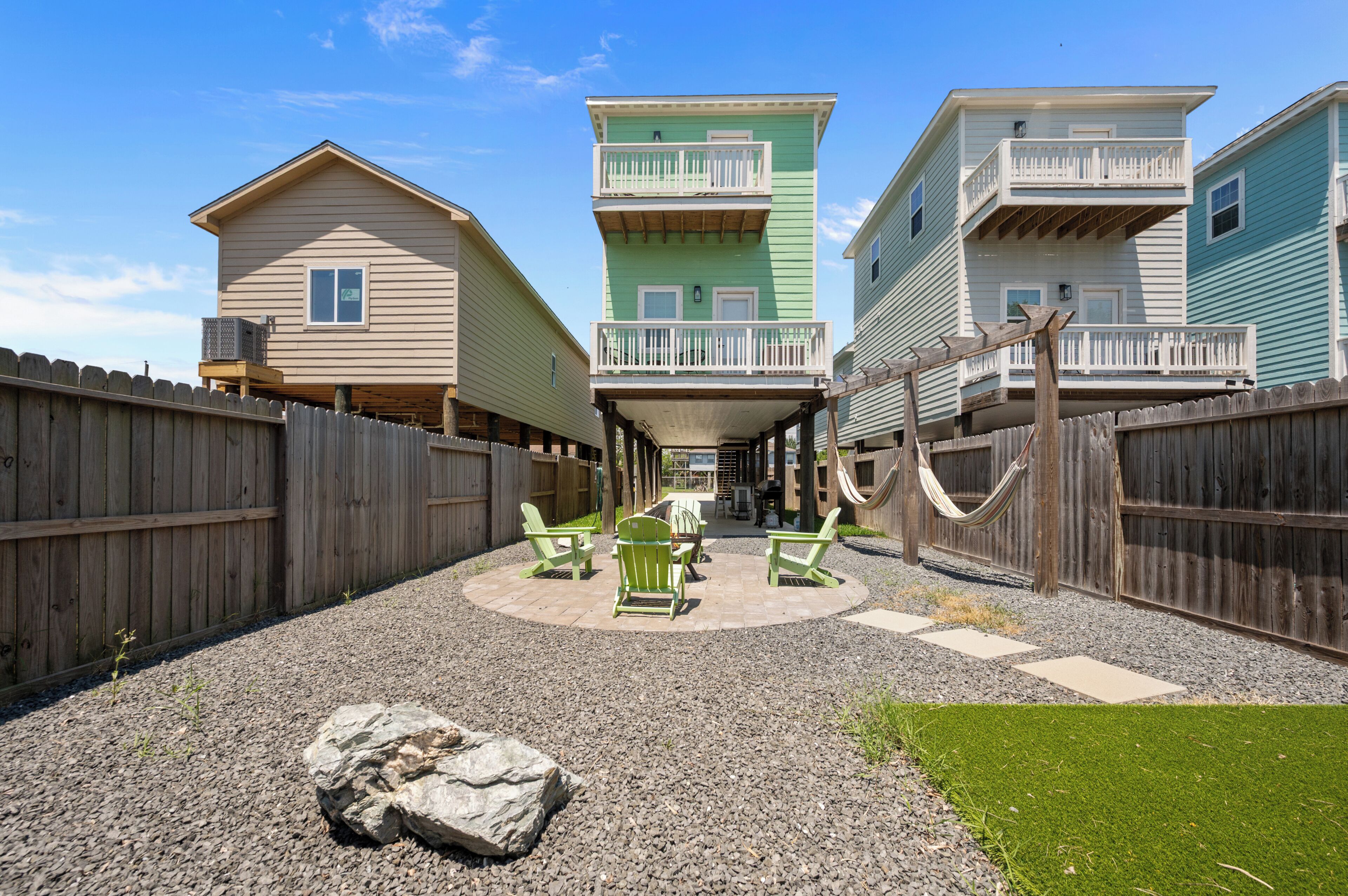 A row of beach houses with balconies, a wooden fence, and a patio area with chairs and a hammock.