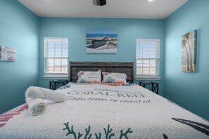 Camera da letto con un letto, due finestre, un quadro raffigurante una barca e un cuscino con la scritta 'CORAL REEF'.