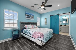 A bedroom with a bed, a ceiling fan, a window, and a bathroom visible through an open door.