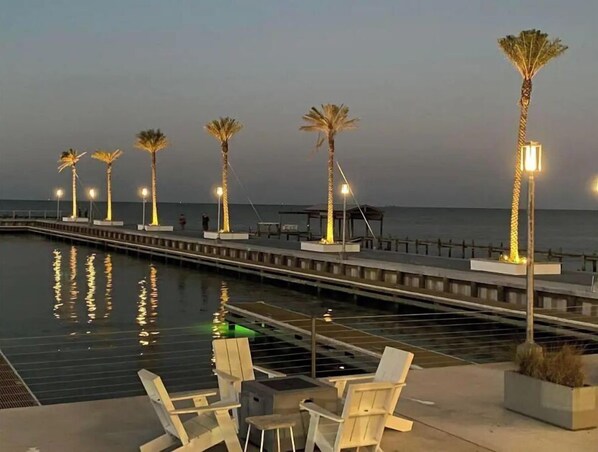 Stroll along the waterfront promenade, surrounded by palm trees and seating areas, with a calm body of water below.