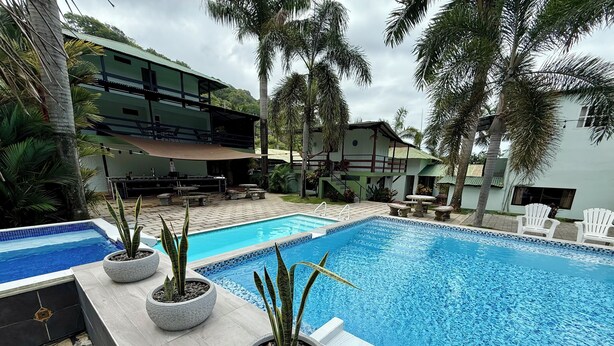 A swimming pool with potted plants, outdoor seating, and a view of a multi-story building. - Cabinas Brisa Del Mar (Jacó)
