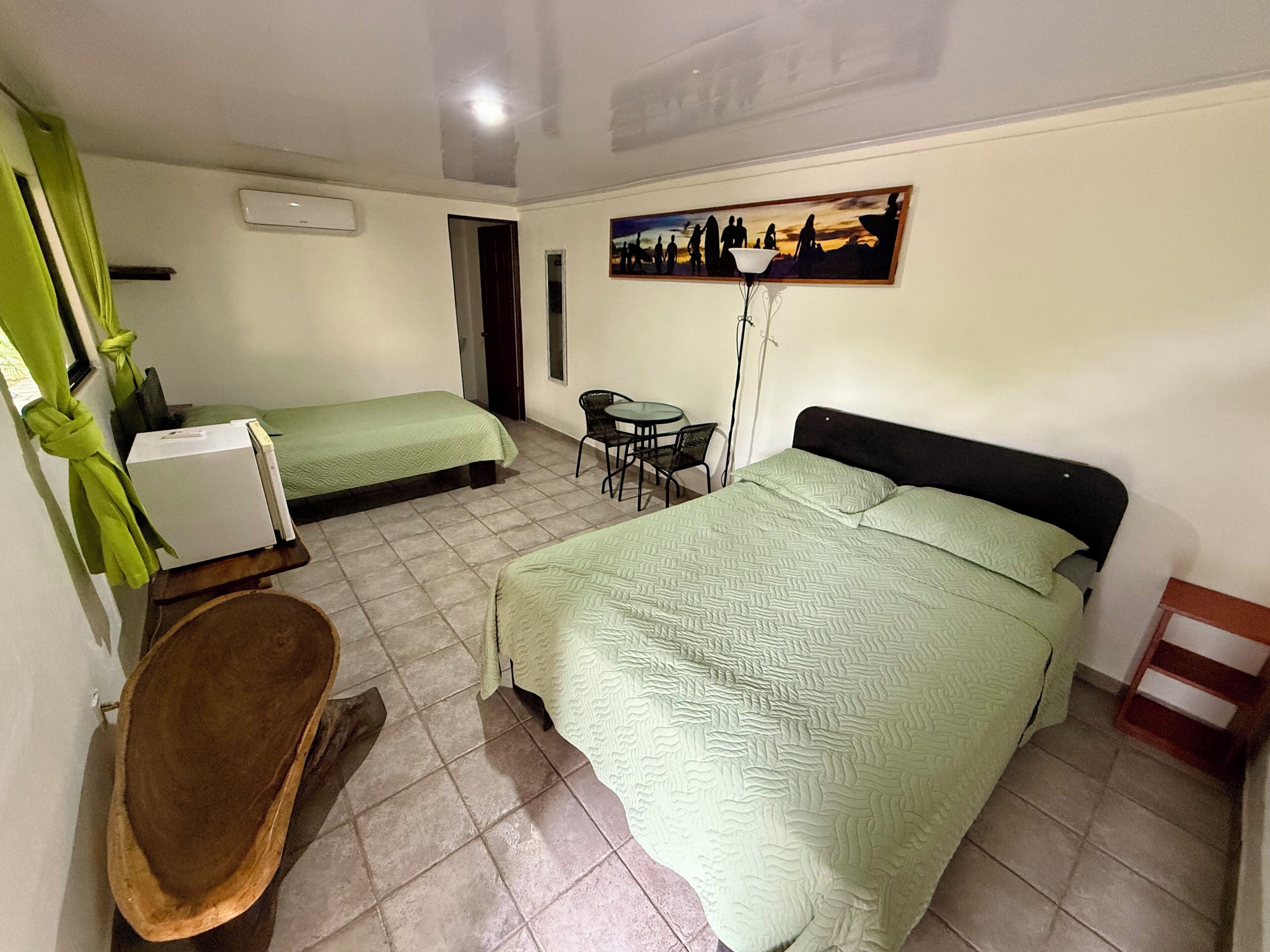 Habitación de hotel con dos camas, un escritorio, una silla, una mesita y un cuadro en la pared.