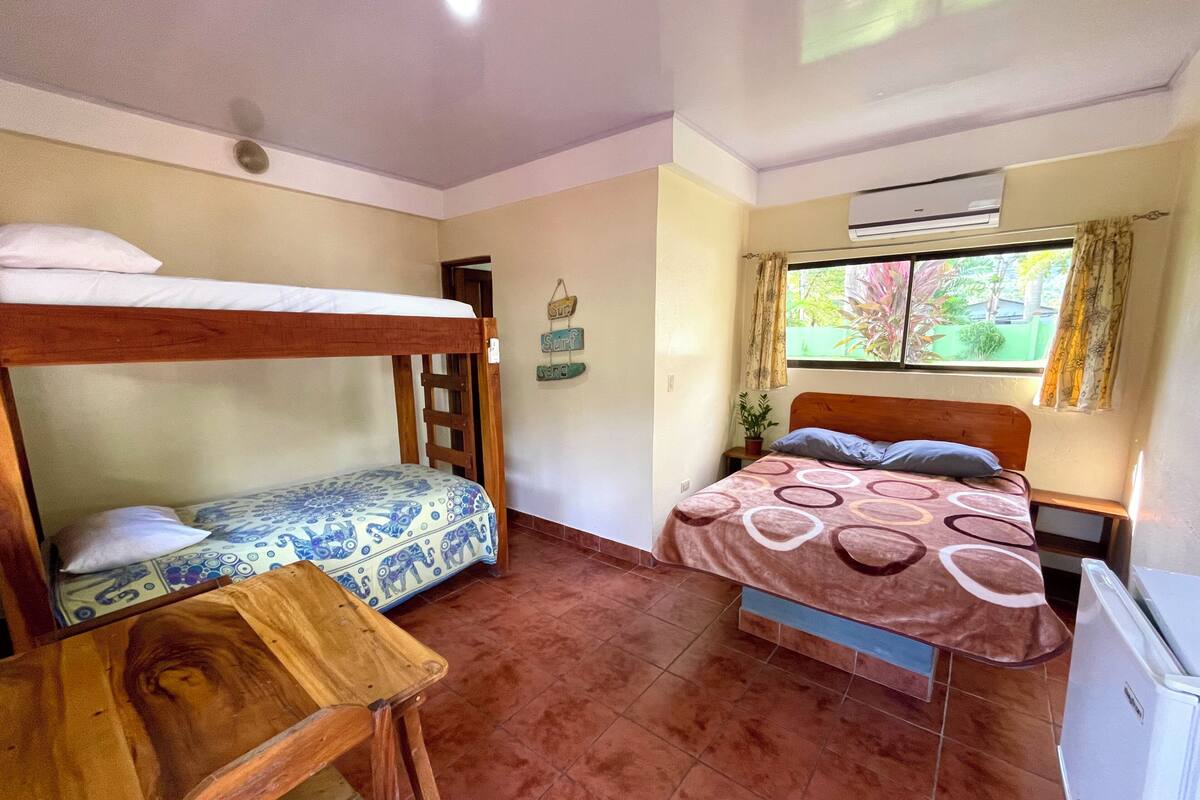 A room with two beds, a wooden table, a potted plant, and an air conditioning unit.