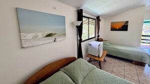 A room with two beds, a window with curtains, a wall-mounted air conditioner, and a painting of a beach scene. - Cabinas Brisa Del Mar (Jacó)