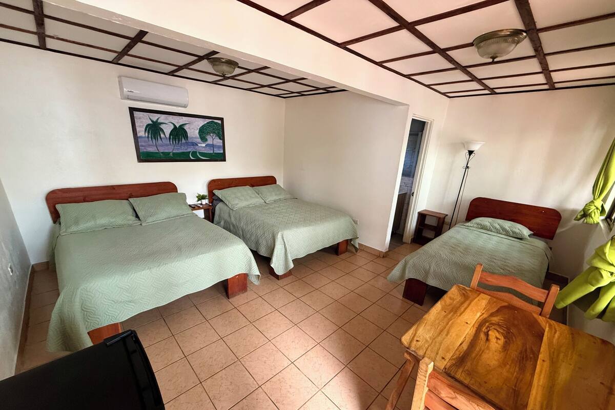 A room with two beds, a desk, a chair, a ceiling fan, and a window with curtains.