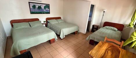 A room with two beds, a desk, a chair, a ceiling fan, and a window with curtains.