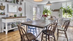 Un comedor rústico con una mesa y sillas de madera, rodeado de estantes con diversos objetos y plantas.