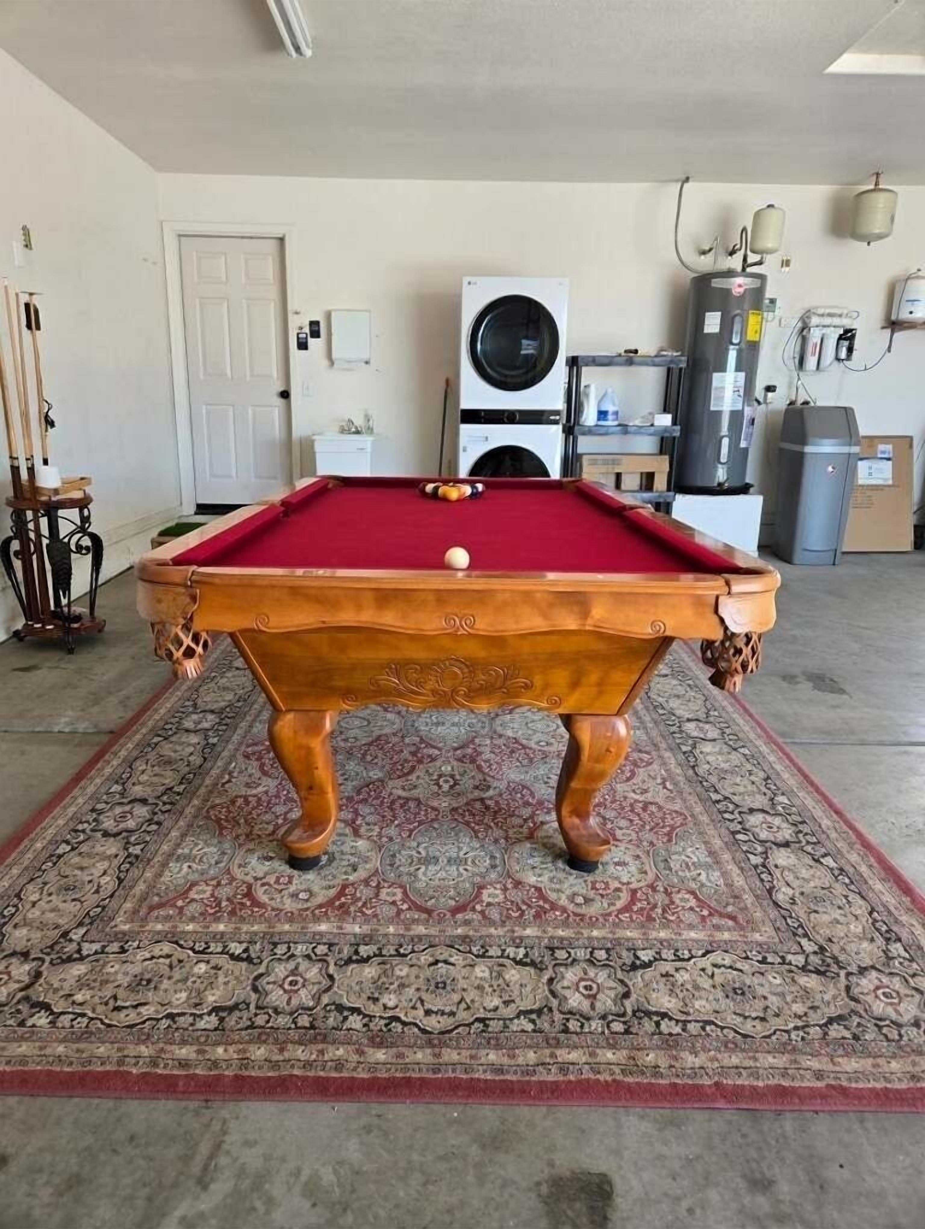A pool table in a room with a patterned carpet, a door, and a washing machine in the background.