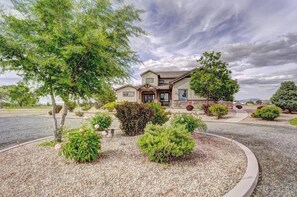 A two-story house with a stone facade, a front porch, and a landscaped garden with various shrubs and a large tree. - Mimosa Fields: Designer Kitchen w/ Outdoor Oasis (Fruita)