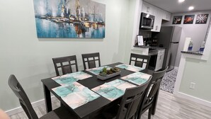 Uma  área de refeições com uma mesa preta, seis cadeiras e um quadro na parede.