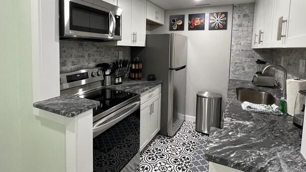 Uma cozinha moderna com armários brancos, eletrodomésticos de aço inoxidável, painel de fundo padronizado e bancada de mármore.
