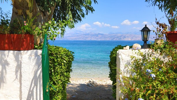 Un sentier de pierres qui mène à une plage d’où l’on a une vue dégagée sur la mer et les montagnes lointaines.