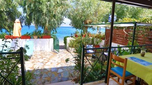 Un espace extérieur abrité, doté d’un sol en pierre, d’une table recouverte d’une nappe jaune et offrant une vue sur la mer.