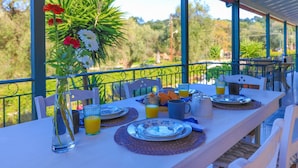A table set for breakfast with plates, glasses, and a vase of flowers on a balcony overlooking greenery. - Villa Valentina in Corfu (Corfu)