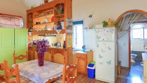 A kitchen with wooden cabinets, a dining table with a lace tablecloth, and a refrigerator with butterfly decals. - The Old Office in Kalami (Corfu)