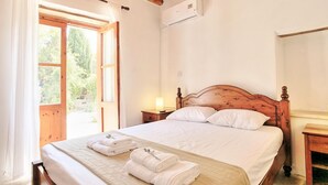 Ein Schlafzimmer mit einem Holzbett, weißen Bettwäsche, einem Nachttisch mit Lampe und einem Fenster mit Vorhängen.