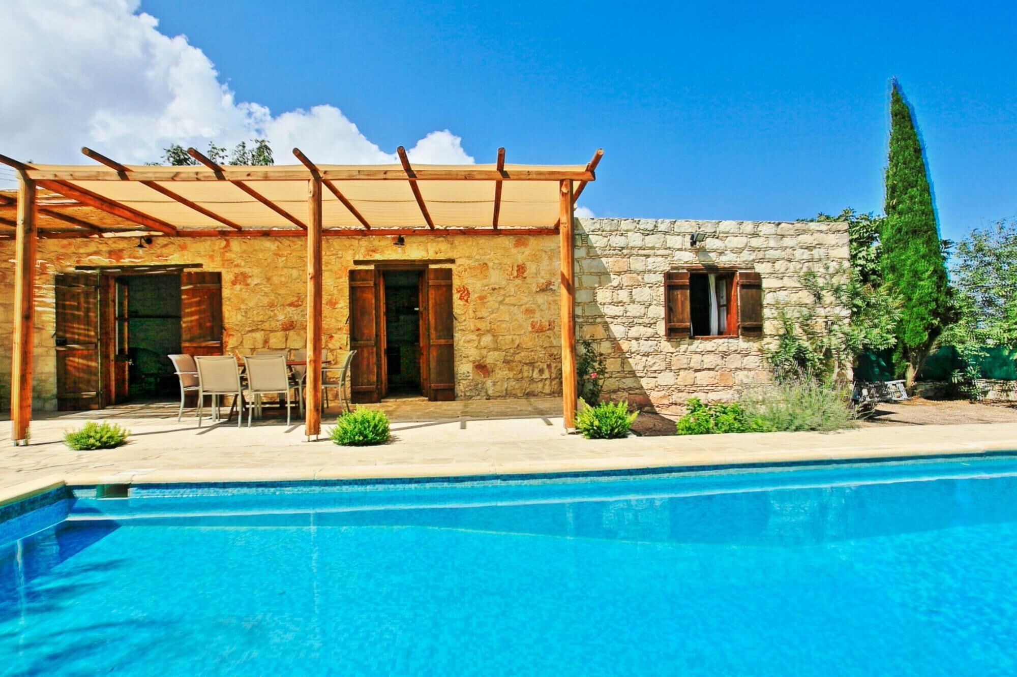 Ein Steinhaus mit Pool, Holz-Pergola und Sitzgelegenheit im Freien.