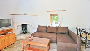 Ein Wohnzimmer mit Holzboden, einem Steinkamin, einer Couch, einem Couchtisch und einem Fernseher auf einer Holzkommode.