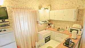 A compact kitchen with white cabinets, a stove, a microwave, and a dining table. - Korinas Cottage in Kentroma (Corfu)