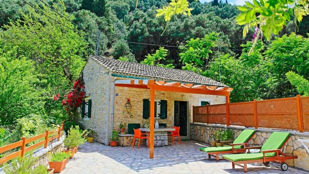 A stone house with a tiled roof, outdoor seating, and a wooden fence. - Korinas Cottage in Kentroma (Corfu)