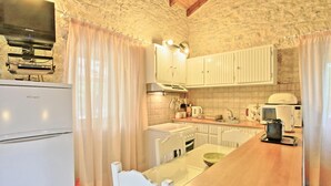 A kitchen with white cabinets, a stove, a refrigerator, and a television mounted on the wall. - Korinas Cottage in Kentroma (Corfu)