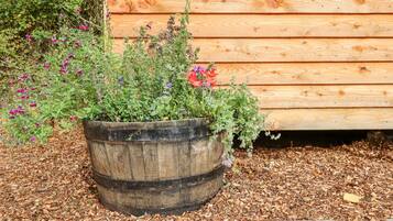 A wooden barrel planter filled with various plants and flowers, placed on mulch, next to a wooden fence.