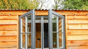 Een houten chalet met een groot raam, voorzien van een zwarte lijst en een zichtbare lichtschakelaar.