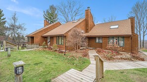 Ein modernes, zweistöckiges Haus mit einer Holzterrasse, einem kleinen Garten und blauem Himmel.