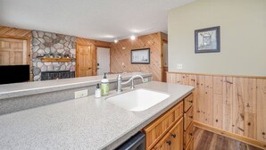 Eine Küche mit Granit-Arbeitsplatten, einem weißen Spülbecken, Holzschränken, einem Kamin aus Stein und einer Wand mit Fischgrätmuster.