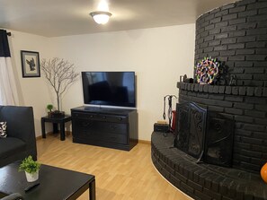 Un salon avec un meuble de rangement noir pour l’équipement audiovisuel, un téléviseur à écran plat, une cheminée et une petite plante posée sur une table basse.