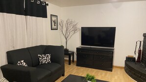 Ein Wohnzimmer mit schwarzem Sofa, Couchtisch, Fernseher und Kamin.