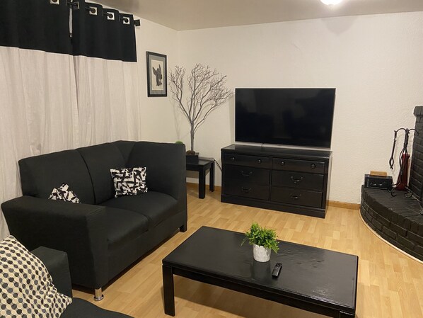 Un salon avec un canapé noir, une table basse, un téléviseur et une cheminée.