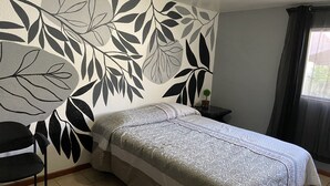 Ein Schlafzimmer mit einem Bett, einem Sessel, einem Nachttisch, einer Wand mit Blättermotiv und einem fenster mit Vorhängen.