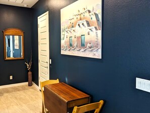 A room with a dark blue wall, a wooden table, a chair, a white door, and a framed painting.