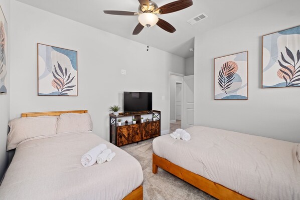 A hotel room with two beds, a ceiling fan, a TV, and artwork on the walls. - Modern Tropical 5 BR/8 BEDS Home in Heart of Dallas (Dallas)