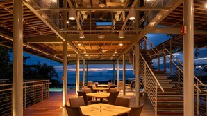 Un espace extérieur aménagé pour les repas, avec des tables et des chaises, une terrasse en bois et un escalier menant à un niveau supérieur.