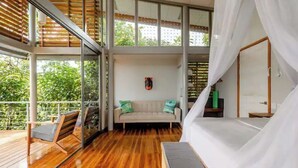 Une pièce spacieuse avec un plancher en bois, un canapé avec des coussins, une grande fenêtre et un balcon doté d’une balustrade en bois.