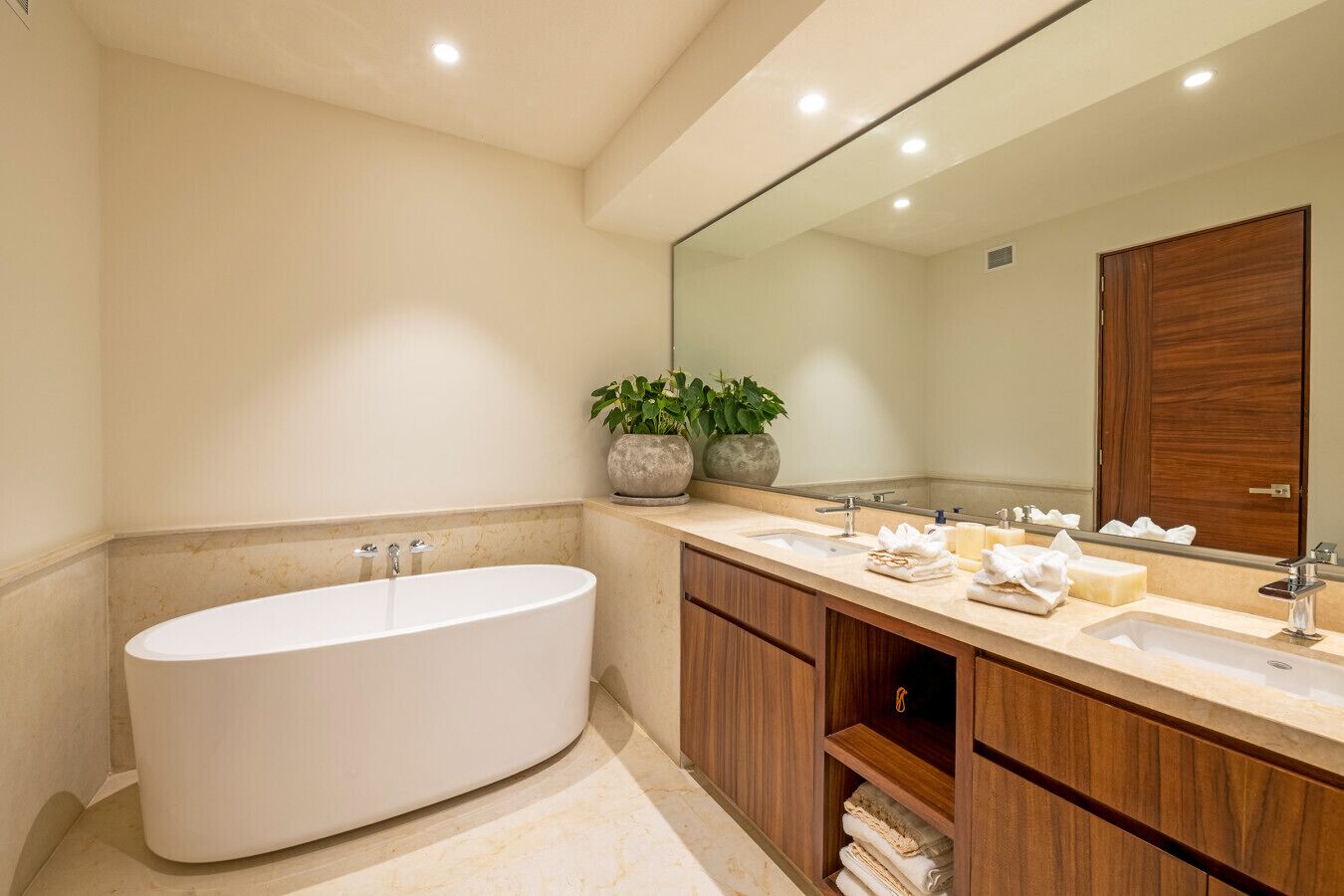 A modern bathroom with a freestanding bathtub, a large mirror, and wooden cabinetry.