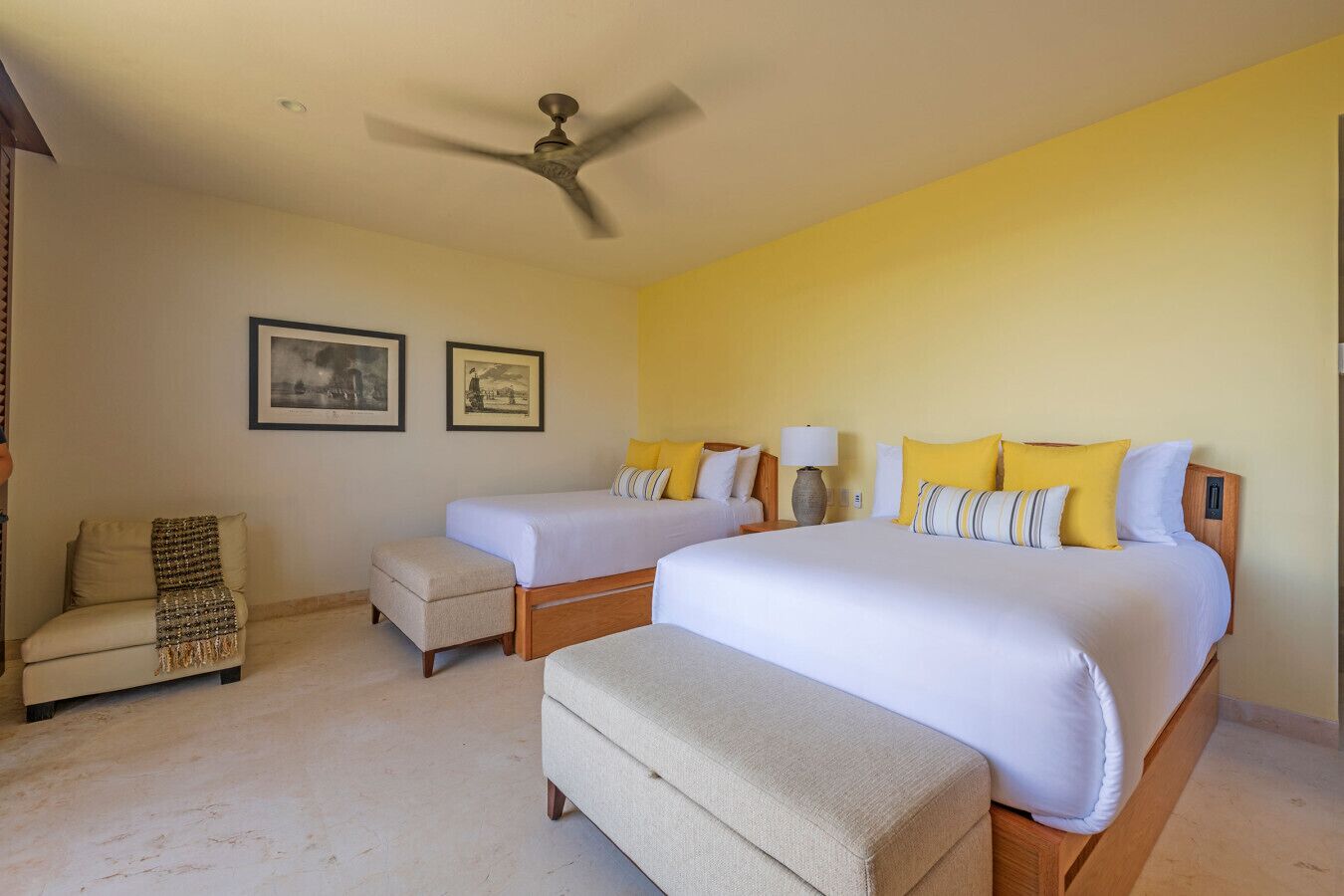 A hotel room with two beds, a ceiling fan, and artwork on the walls.