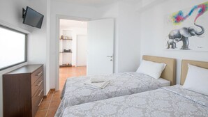 A hotel room with two beds, a TV mounted on the wall, and a colorful elephant painting. - Kalma Villa Ena in Moudania (Nea Propontida)